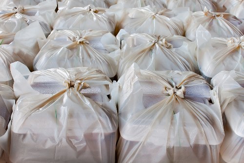 A large group of tightly packed white rubbish bags made of glossy plastic material, each tied securely at the top with a twist tie or knot, arranged closely together in an outdoor setting. The bags are on a paved or concrete surface, with some bags layered behind others, occupying the foreground and middle ground. The environment appears to be an open area, possibly a driveway or parking space near commercial premises. The surface is neutral in tone, with no visible background structures or distinctive features. The image conveys the concept of waste ready for collection, consistent with rubbish removal services like those offered by Commercial Waste Potters Bar, in a typical urban or suburban context. The visual emphasizes the accumulation of waste awaiting collection, reflecting the volume handled by professional rubbish disposal providers.